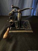 Side angle showing the fluted rollers, hand crank with wooden handle, and iron frame