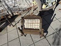 Front view showing brass tone gas heater with wire mesh screen and ornamental top sign with brand name readable.