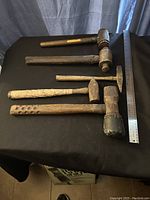 Top view showing all five heavy hammers lined out on dark surface with measuring ruler beside them for scale