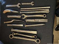 Complete assortment of vintage tools laid out on a black surface including wrenches, chisels, bits, and a knife-shaped handmade tool.