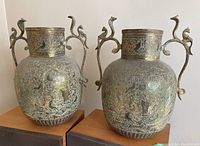 Front view of the two brass vases standing side by side on a wooden surface showing overall shape, detailing, and cobra handle designs.