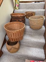 Full group of five baskets arranged on carpeted stairs showing size range and variety of weave and design.