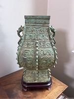 Frontal view of four-sided bronze vase on wooden stand showing overall shape and decorative motifs