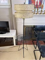 Full front view of black iron tripod base, circular wire side table and two-tiered cream and brown textured shade.
