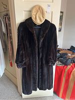 Full view of dark brown fur coat hanging on a door with beige captain style hat on top