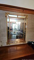 Overall front view of mirror hanging on wall above wooden surface, showing full frame and mirror plate.