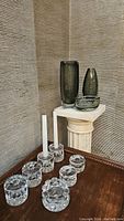 Three smoky gray Orrefors vases on pedestal and seven clear crystal faceted candlestick holders on table.