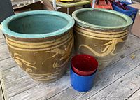 Two large ceramic pots with yellow dragon designs and turquoise rims alongside a smaller blue ceramic pot with a red interior and a medium-sized metal pot with handle on wooden floor.