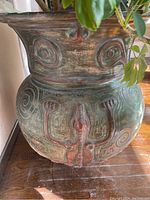 Close-up of pot front showing embossed reptile body design with red and green patina