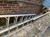 Two aluminum ladders outdoors resting against brick wall amid leaves and dirt; closer view of feet and ladder rungs shows green rubber caps and metal construction.