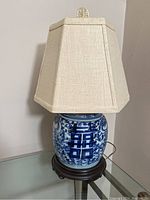 Full view of the lamp showing the porcelain base, fabric shade, and wooden stand.