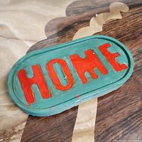 Oval jesmonite tray in teal color with raised red letters 'HOME' shown on a reflective surface.