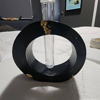 Front view of black circular jesmonite vase with clear glass tube and gold leaf accents