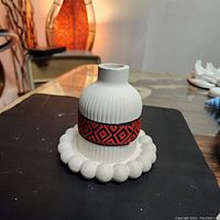 Front angled view of the handmade white jesmonite decorative vase with red and black fabric band, set on a white beaded tray.