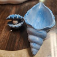 Decorative blue clam shell with pearl inside, positioned beside the box holder for scale and context.