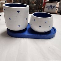 Front view of the tray with two handmade jesmonite boxes, showing white exteriors with blue hearts and solid blue interiors on an oval tray.