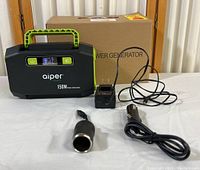 Front view of Aiper 150W portable power station with wall charger, car charger with cable, and car cigarette lighter adapter in front, and original box behind