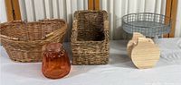 Photo showing large wicker basket with handles, smaller rectangular basket, metal round basket, glass jar, and wooden pumpkin