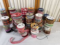 Photo of multiple spools of mixed Christmas and other themed ribbons arranged in rows, showing variety of colors and patterns