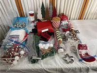 Photo showing a wide spread of Christmas crafting and decoration items including beaded berry picks, tinsel garland, small wooden trees, ribbons, candy cane decorations, stocking, and other supplies on a white table.