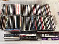 Full view of approximately 70 music CDs arranged horizontally in a plastic container, showing spine labels with various artists and album titles.