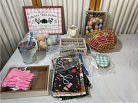 Overview of Easter themed crafting and decoration items on table including sign, eggs, fabrics, gloves, watering can, creamer, crate organizer, jar, and tray.