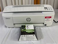 Front view of white HP DeskJet 3755 printer with HP 65XL and HP 65 ink cartridge packaging placed in front, showing model and branding.