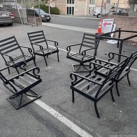 Photo of six black metal outdoor patio chairs arranged in a circle with a metal table frame, showing condition and design of seats and table frame without glass top.