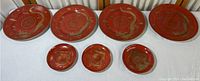Seven red and gold dragon decorated porcelain plates displayed on a white cloth surface.