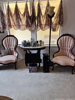 Full view of the two antique parlor chairs and marble-top side table in a sitting area with window behind them.