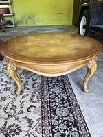 Front angle view of vintage round wood coffee table showing smooth polished top and ornate curved legs.