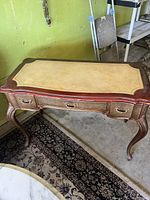 Photo of antique wooden desk showing three drawers, leather top inset, and cabriole legs with decorative handles.