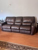 Full view of the brown leather reclining couch showing three cushioned seats with two recliners on the ends