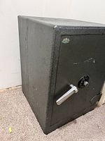 View of closed vintage fire safe showing metal handle and combination dial on front door.