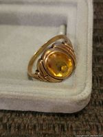 Close-up of the ring showing yellow cabochon gemstone and gold band details.