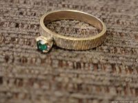 Close-up photo of the 14k gold ring showing textured band and small green stone.
