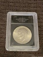 Obverse side of the 1976 Eisenhower Silver Dollar coin in plastic case showing Eisenhower's profile with inscription and certification label.