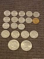 Top view of multiple Roosevelt dimes and one copper-colored penny arranged on a fabric surface showing coin faces.