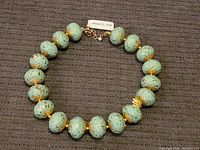 Full view of the chunky necklace showing large mint green beads with gold-tone floral caps and gold chain closure.