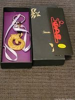 Full view of the yellow carved snow jade pendant on keyring inside black branded box with ribbon and beads.