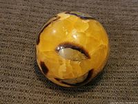 Polished multi-stone sphere with yellow, beige, brown, and black patterns from front angle showing the colors and glossy finish.