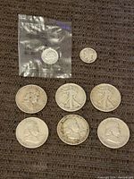 Lot of 8 coins laid flat on textile surface, including half dollars, dimes, and nickel.