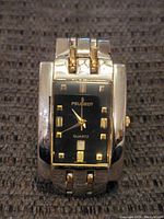 Front view of gold tone Peugeot watch with black dial, gold numeral markers, and date window.