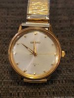 Front view of Seiko men's wristwatch showing white dial with gold hour markers and hands.