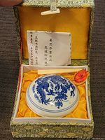 Top-down photo of the porcelain inkstone with blue dragon design inside a decorative box with certificate and wooden stick.