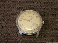 Front view of vintage Gruen Precision men's watch showing white dial with Arabic numerals and gold-tone hands, with signs of wear and scratches on dial and crystal.