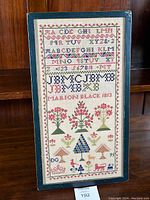 Full view of framed sampler replica showing alphabets, numbers, name, and decorative motifs.