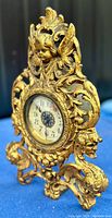 Angled view of the gold ornate cast iron antique clock showing cherub and detailed scrollwork