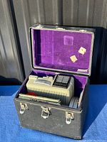 Eumig P8 projector in original hard case with purple velvet inside, showing projector and some film reels in storage.