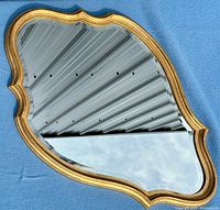 Top-down view of the vintage mirror showing the ornate gilded frame and beveled curvilinear glass surface.